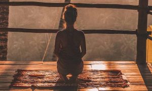 woman facing backward sits focusing on meditation on balcony