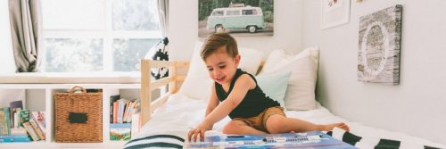 little adorable boy sits on bed excitedly read kids children book in tidy cozy bedroom