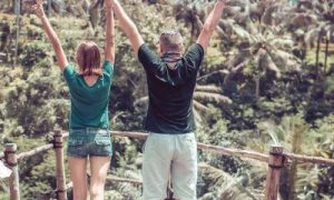 couple stands on bridge in forest raising hands gratitude life