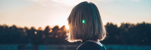 short hair woman facing backward stands looking at sunny sky