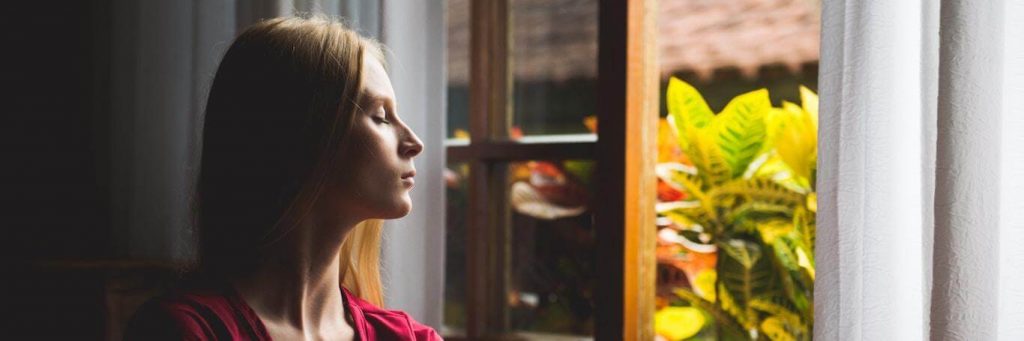 woman sits beside open window eyes closed thinking