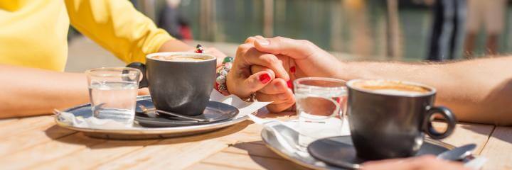 hands holding beside two coffee cups two glasses of water