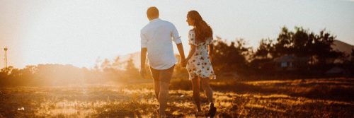 couple holds hands walking on field in sunny sky