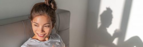 woman sits on bed holding glass of water smiling