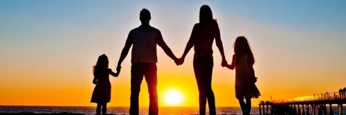 happy family stands hand in hand beside ocean sea cliff watching breathtaking sunset scene