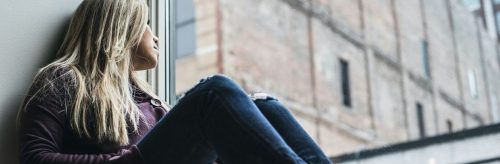 woman sits next to window looking at tall old building