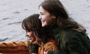 two women stands on snow hugging happily smiling pointing