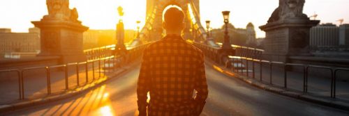 man facing backward walks along bridge in sunny sky