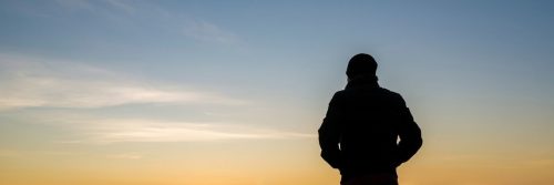 man shadow stands facing backward looking at red blue partially clear sky