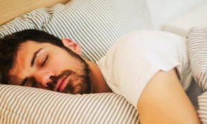 man sleeps tightly on bed covering body with stripped blanket