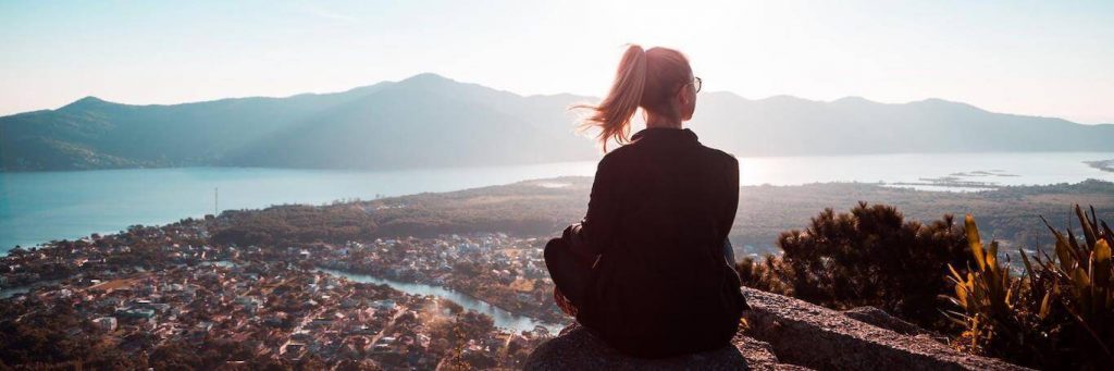 woman sits on rock enjoying nice weather looking at mountain blue sunny sky