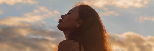 woman eyes closed focuses on breathing in blue cloudy sky