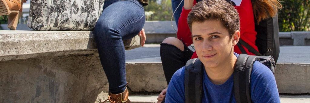 young man sits on stairs smiling in university campus