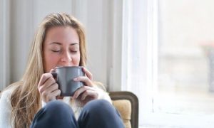 woman sits on chair holding grey mug enjoying drink in living room