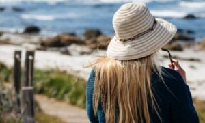 woman facing backward walking along coastal walk beside blue ocean rocks