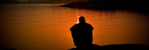 person sits alone beside lake feeling sad in quiet environment