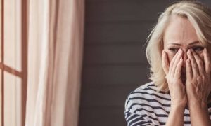 woman hands on face crying worrying feeling hurt sitting beside window