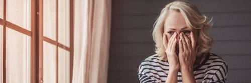 woman hands on face crying worrying feeling hurt sitting beside window