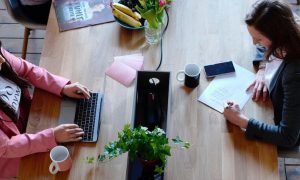 two women sit in co working office working studying beside fresh fruit plate plant pot coffee mug