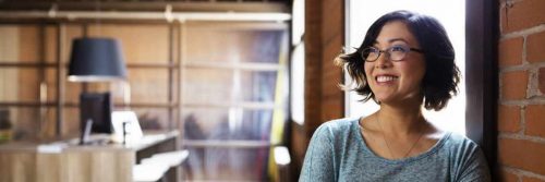 short hair woman stands beside wall smiling in workplace office room