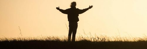 man stands facing backward on field gratitude life in red clear sky