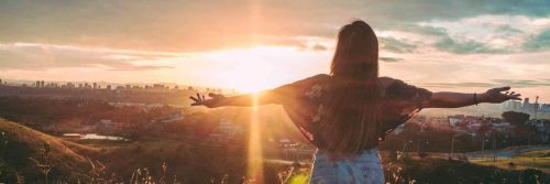 woman stands facing backward gratitude life in beautiful sunny sky