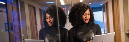 curly black hair woman stands in office working looking at tablet