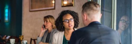 curly black hair woman sits in coffee shop seriously talking to college