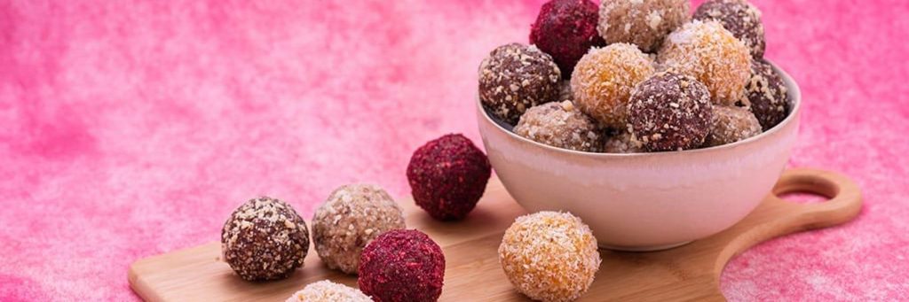 healthy food bowl bliss balls on wood chopping board in pink background