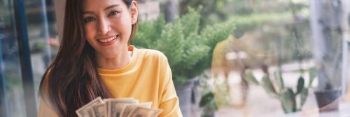 woman holding cash counting money sitting beside window smiling