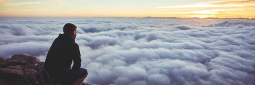 man sits on rock watching clouds beautiful sunset