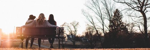 three women sitting on bench facing backward watching sunset