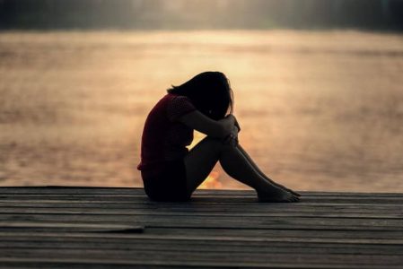 woman sadly sits beside beach head on knees crying