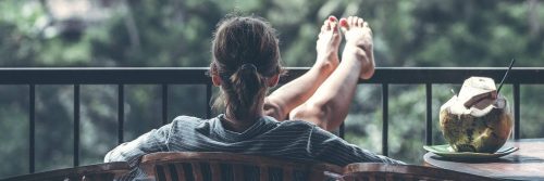 woman sits on chair in balcony drinking coconut water looking at forest