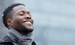 man wearing grey scarf happily smiles enjoys snow weather