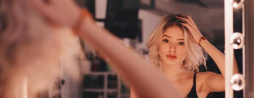 woman scratches hair looking herself in mirror