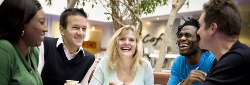 group of mixed genders sit next to coffee shop in shopping mall talking happily laughing