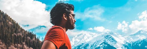 man stands looking at mountain in blue cloudy sky