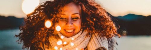 curly hair woman wearing white scarf happily smiles stands opposite to mountain