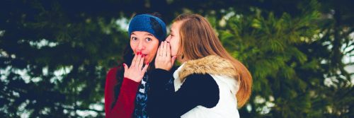 woman whispering to friend while lady surprises