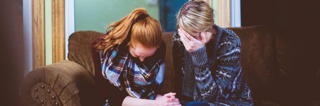 two women sit on couch feeling sad while mom covering face with hand