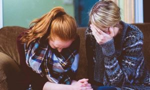 two women sit on couch feeling sad while mom covering face with hand