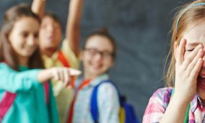 girl hands on face sadly cries while friends bullying pointing laughing at her