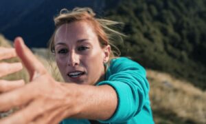 Woman with blonde hair in a green shirt holding her hand out for help