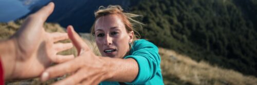 Woman with blonde hair in a green shirt holding her hand out for help