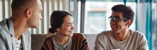 two men one woman sits in office happy faces smiling talking to each other