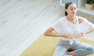 woman sits on yellow rug focusing on breathing meditation practicing calmness