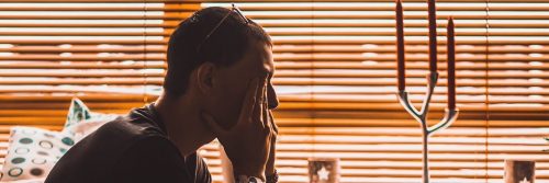 man sits hand in face in living beside candle feeling sad