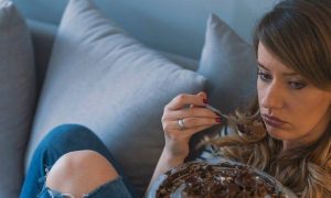 woman sits on couch sadly tiredly eating chocolate bowl