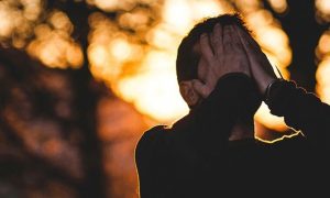 man stands hands in face feeling sad shameful in forest in sunny sky